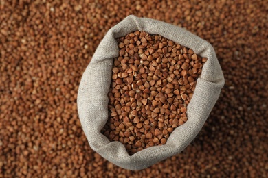 Photo of Uncooked buckwheat in sackcloth bag on grains, top view