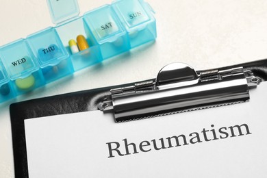 Photo of Clipboard with word Rheumatism and pills on white background, closeup
