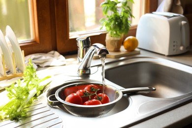 Photo of Fresh ripe tomatoes under tap water in kitchen sink