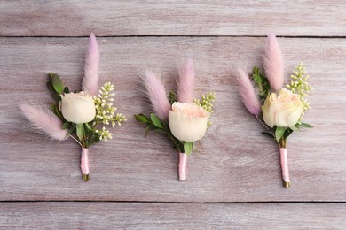 Many small stylish boutonnieres on light wooden table, flat lay