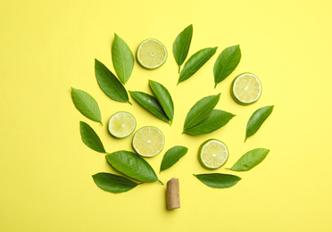 Flat lay composition with fresh green citrus leaves and lime slices on yellow background