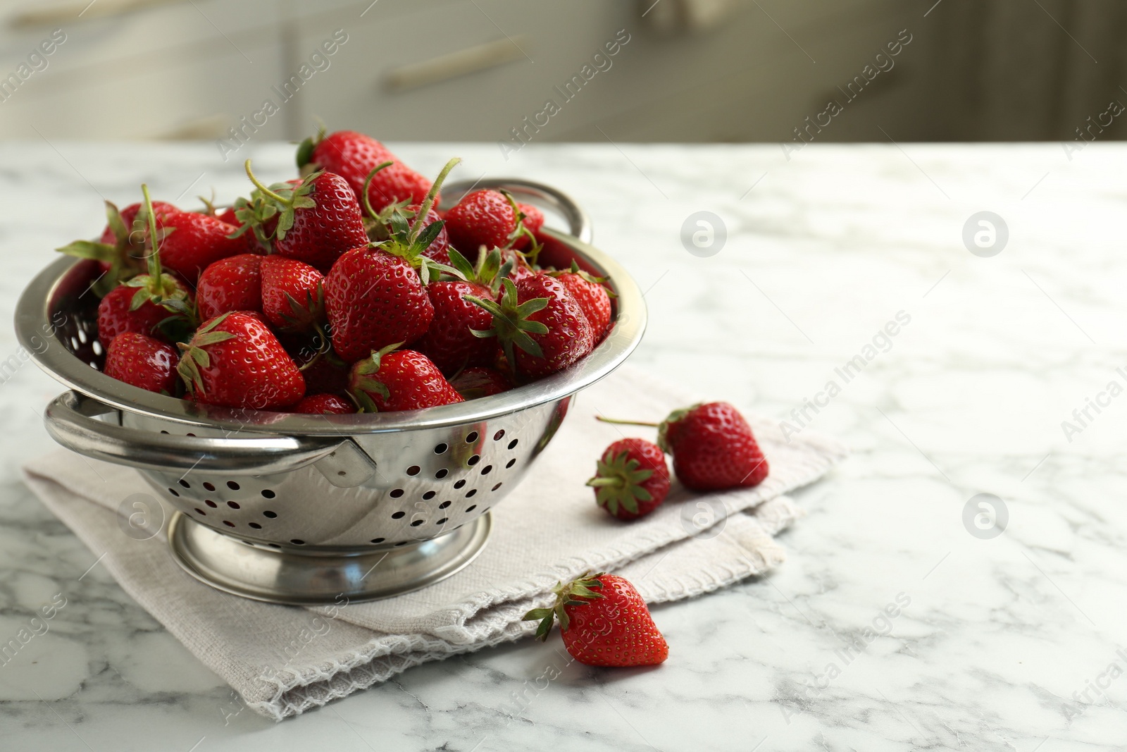 Photo of Metal colander with fresh strawberries on white marble table indoors, space for text