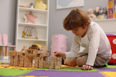 Photo of Little boy playing with wooden construction set on puzzle mat in room. Child's toy