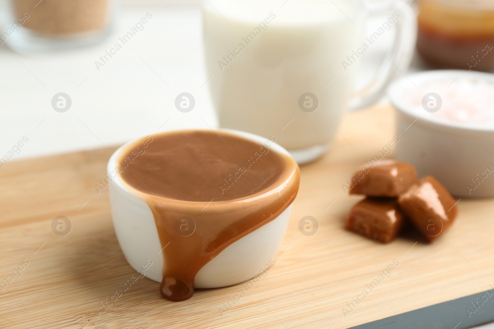 Photo of Bowl with caramel sauce and candies on board, closeup