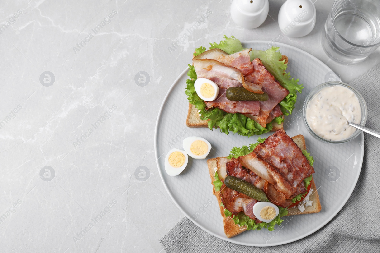 Photo of Tasty sandwiches with bacon and quail eggs served on grey table, flat lay. Space for text
