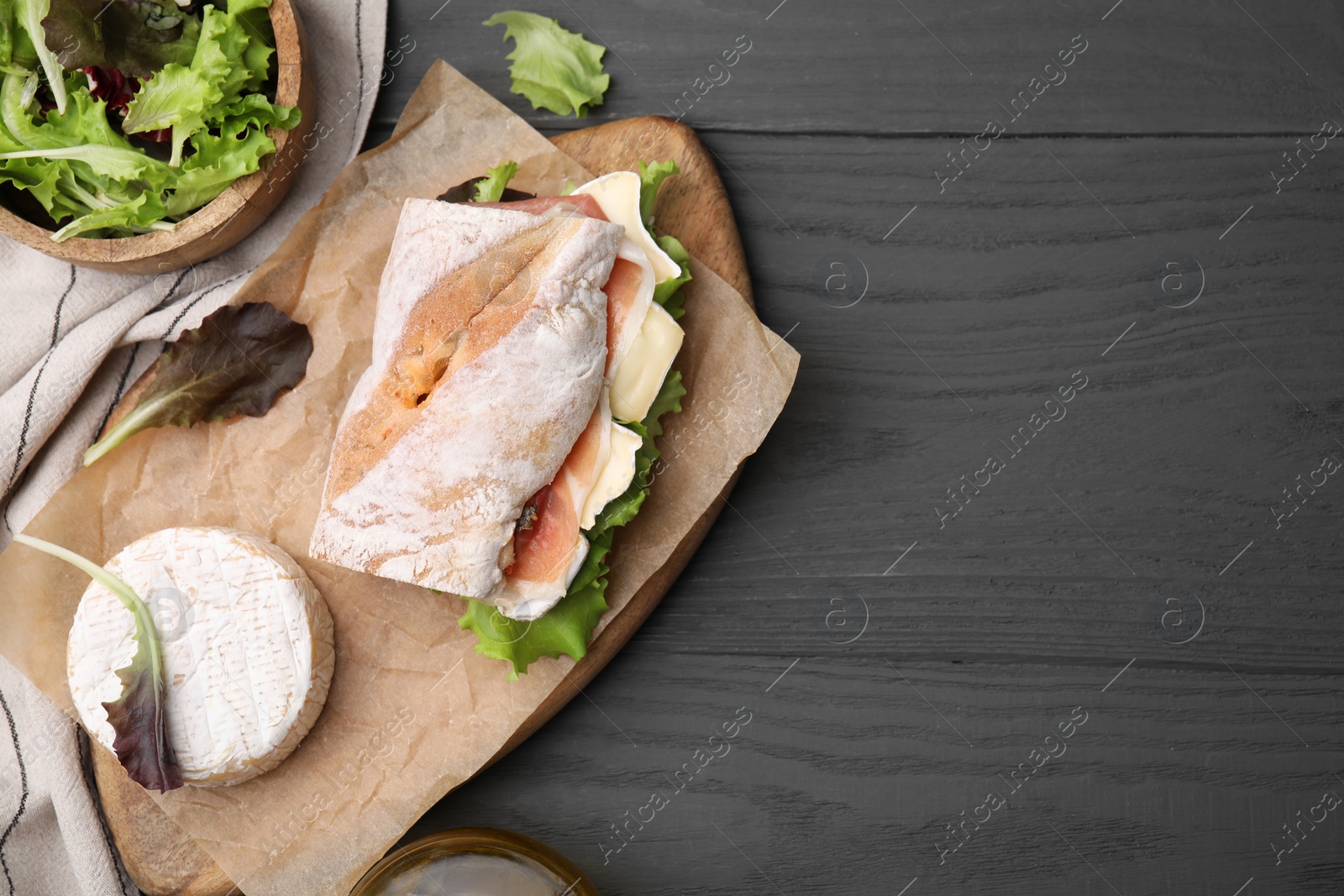 Photo of Tasty sandwich with brie cheese and prosciutto on grey wooden table, flat lay. Space for text