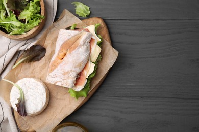 Tasty sandwich with brie cheese and prosciutto on grey wooden table, flat lay. Space for text