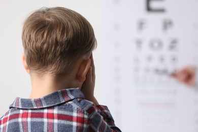 Photo of Ophthalmologist testing little boy's vision in clinic, back view