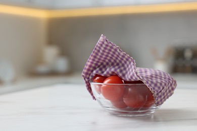 Photo of Tomatoes in bowl covered with beeswax food wrap on white table indoors, space for text