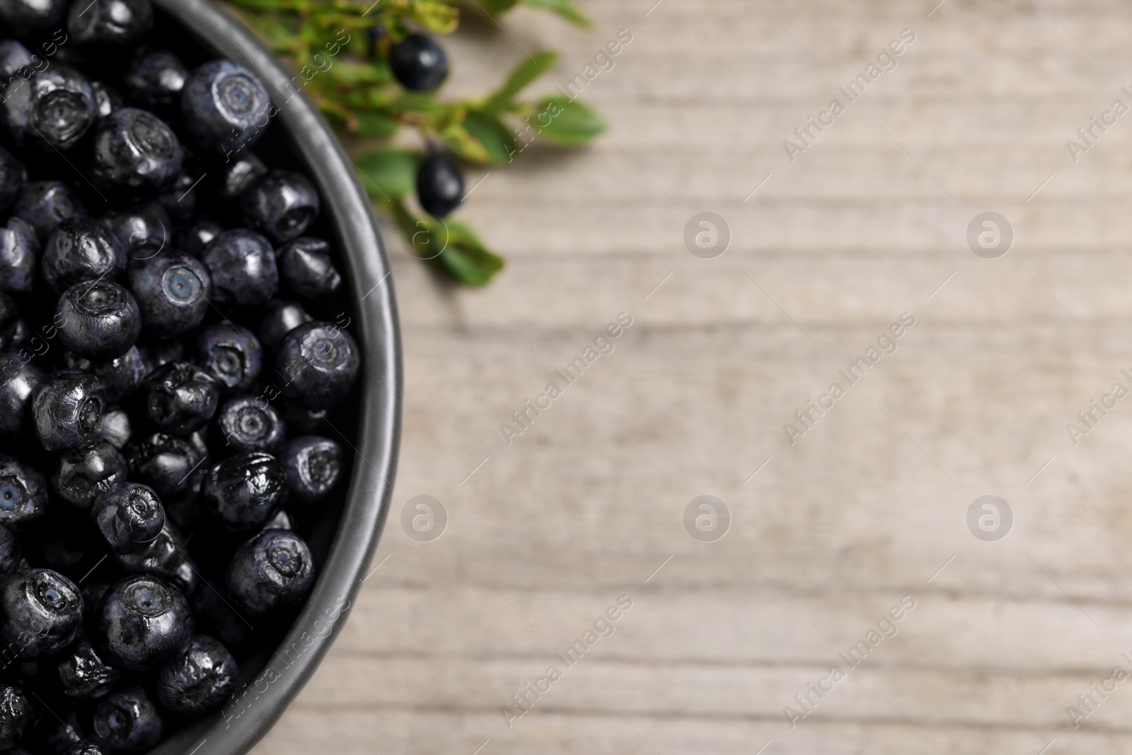 Photo of Ripe bilberries in bowl on wooden table, flat lay. Space for text