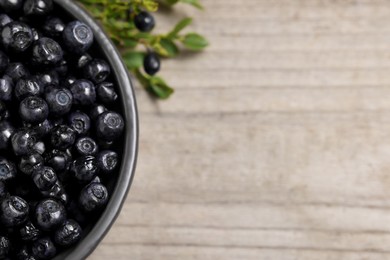 Ripe bilberries in bowl on wooden table, flat lay. Space for text