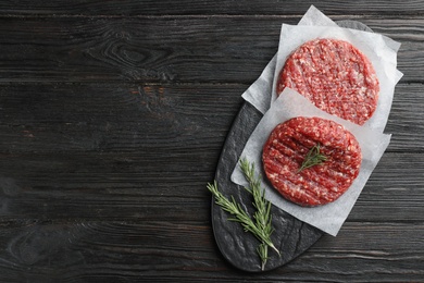 Photo of Raw meat cutlets for burger on black wooden table, top view. Space for text