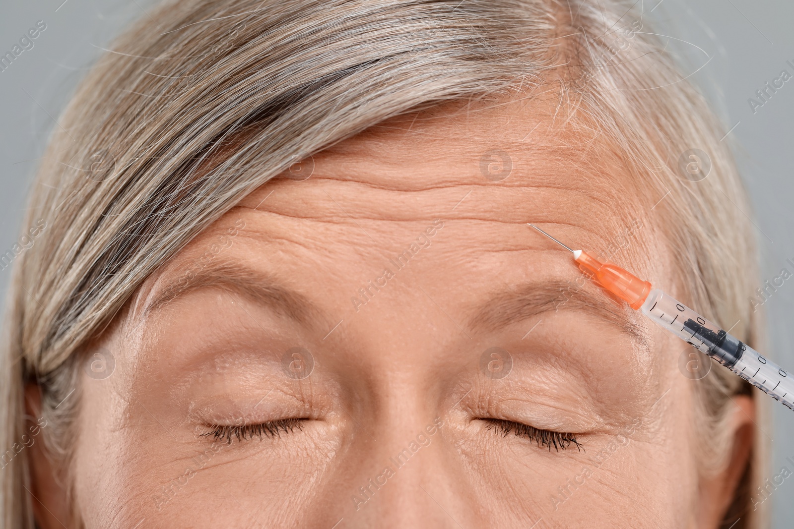 Photo of Senior woman getting facial injection on light grey background, closeup. Cosmetic surgery