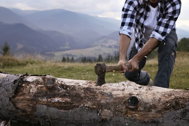 Photo of Man with axe cutting tree log in mountains, closeup