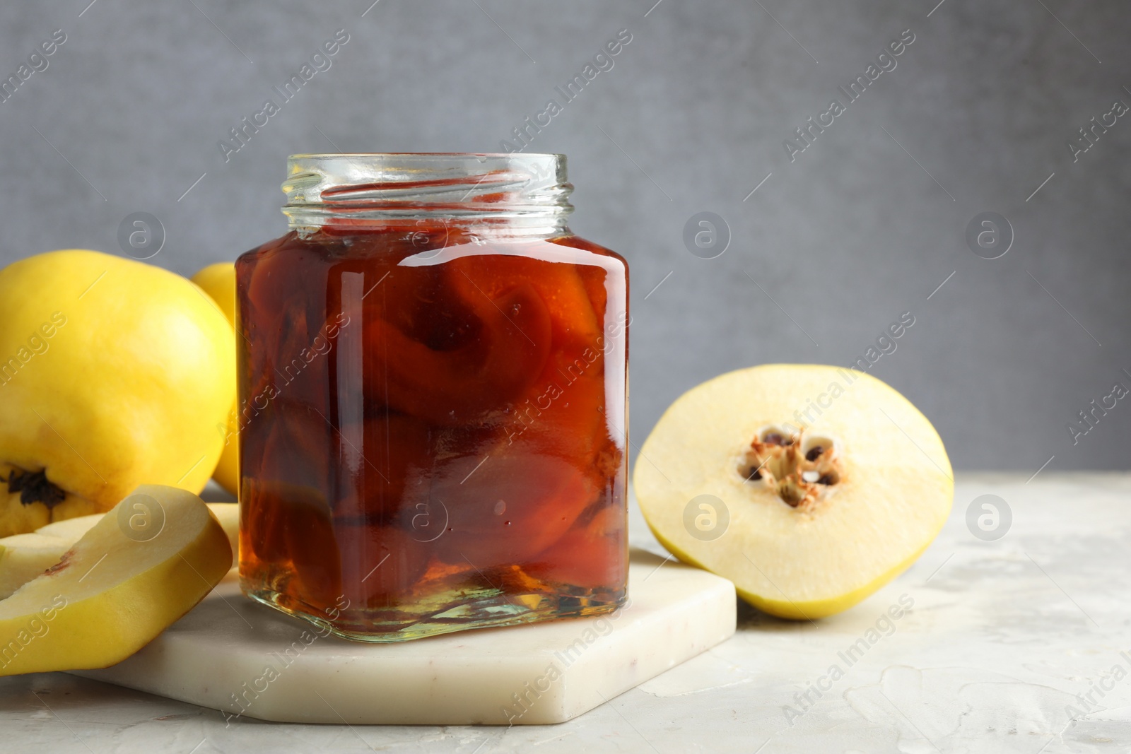 Photo of Tasty homemade quince jam in jar and fruits on grey textured table, closeup. Space for text