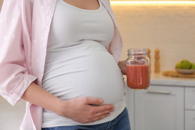 Photo of Young pregnant woman with smoothie in kitchen, closeup. Healthy eating