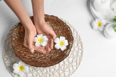 Photo of Woman soaking her hands in bowl with water and flowers on wooden table, above view. Spa treatment