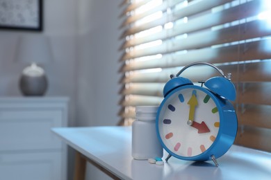 Photo of Alarm clock and pills on white table indoors, space for text. Insomnia treatment