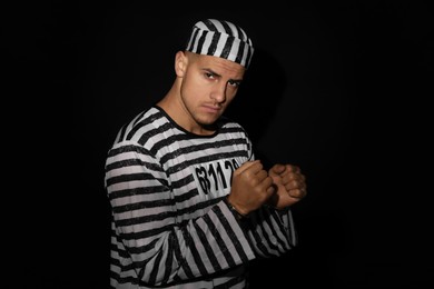 Photo of Prisoner in striped uniform with handcuffs on black background