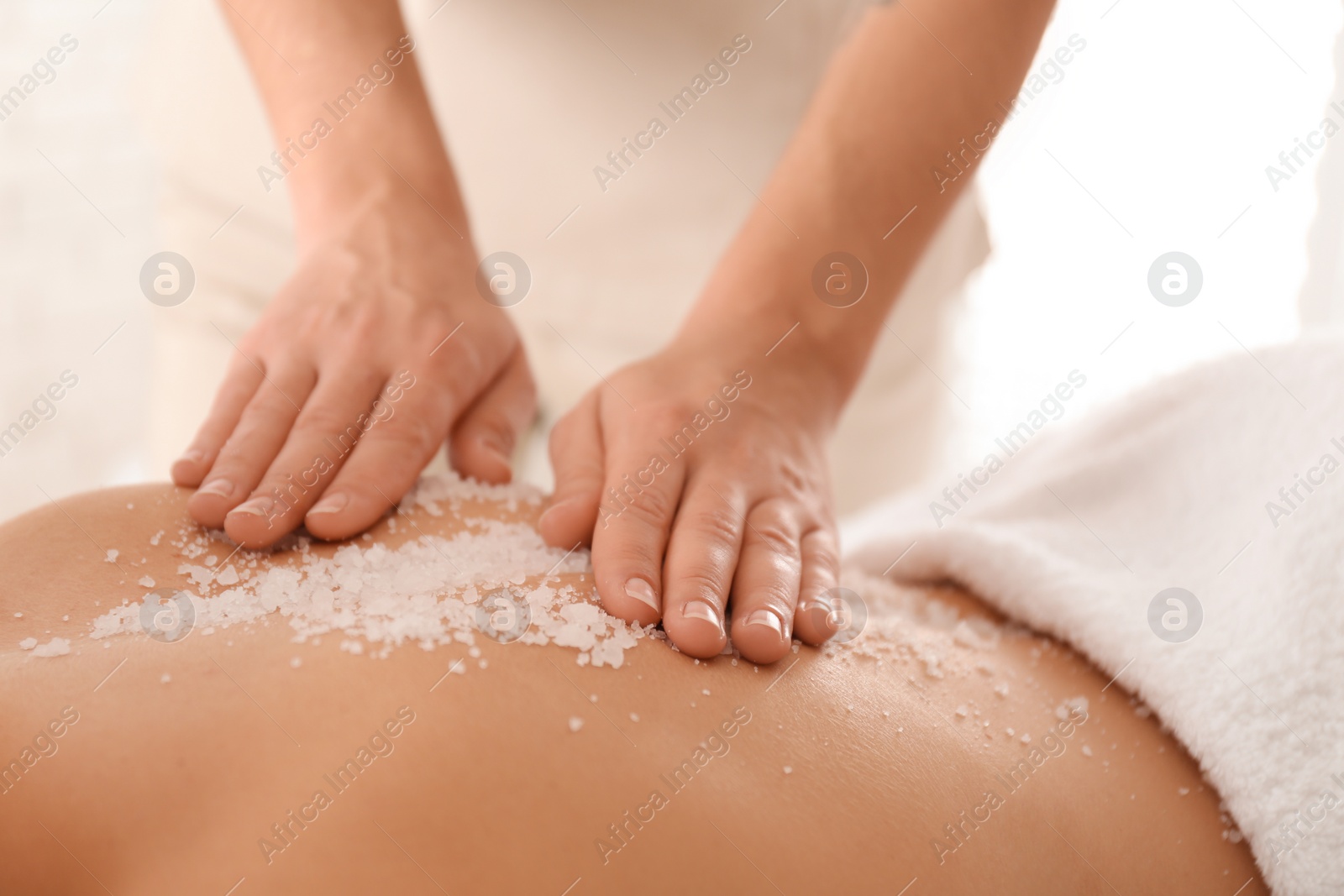 Photo of Young woman having body scrubbing procedure with sea salt in spa salon, closeup