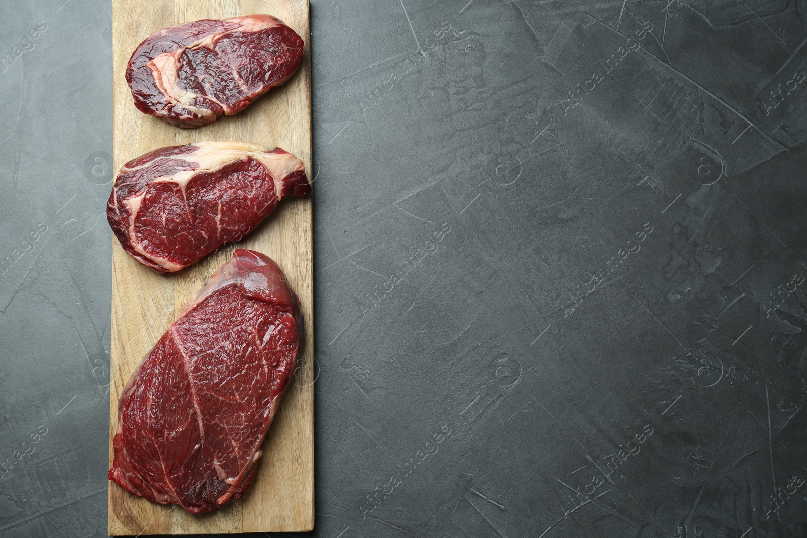 Photo of Wooden board with pieces of raw beef meat on grey table, top view. Space for text