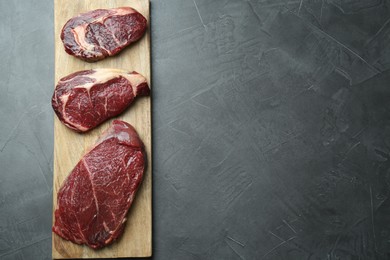 Wooden board with pieces of raw beef meat on grey table, top view. Space for text