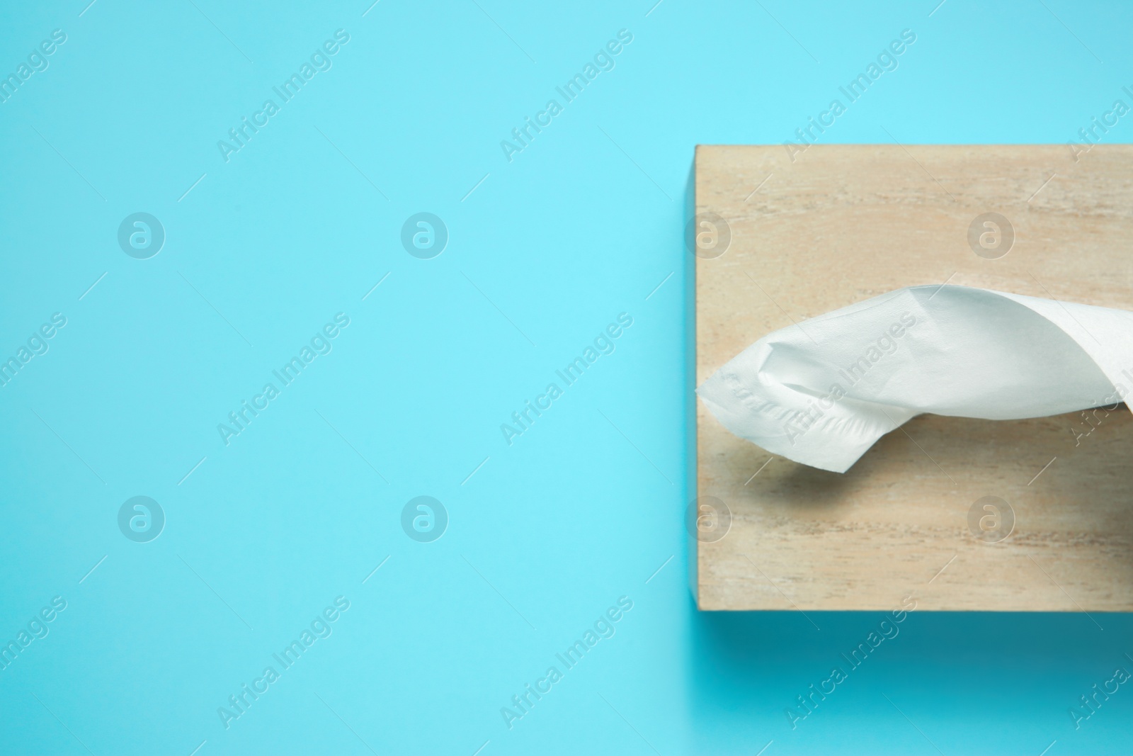 Photo of Wooden holder with paper tissues on light blue background, top view. Space for text