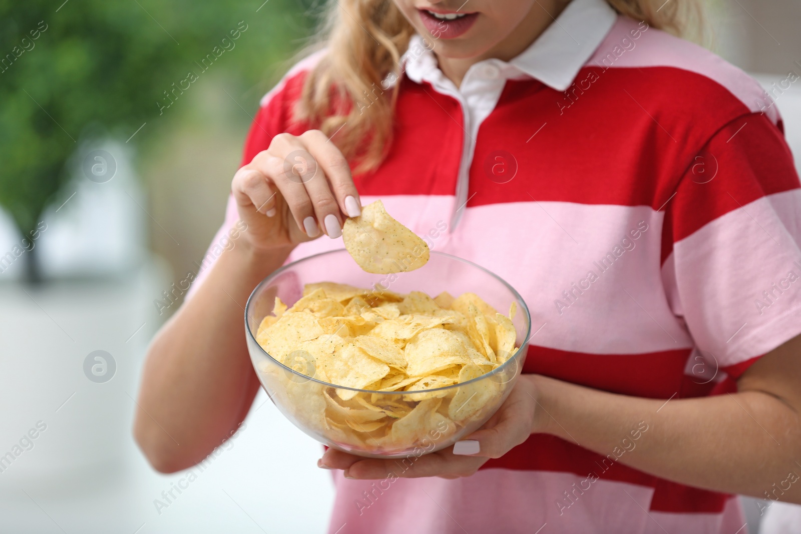 Photo of Woman with bowl of potato chips on blurred background, closeup