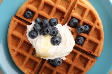 Tasty Belgian waffle with blueberries, honey and whipped cream on plate, top view