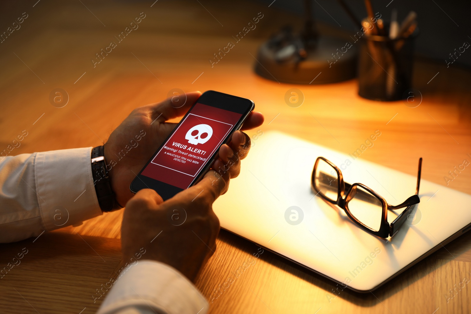 Photo of Man holding smartphone with warning about virus attack at table, closeup