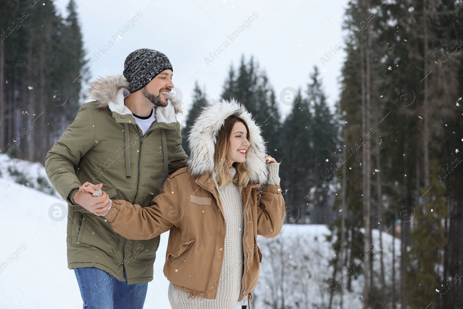 Photo of Happy couple near conifer forest on snowy day, space for text. Winter vacation