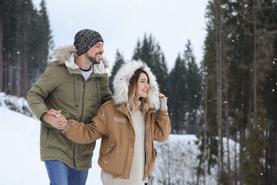 Photo of Happy couple near conifer forest on snowy day, space for text. Winter vacation