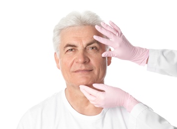 Doctor examining man's face before plastic surgery operation on white background
