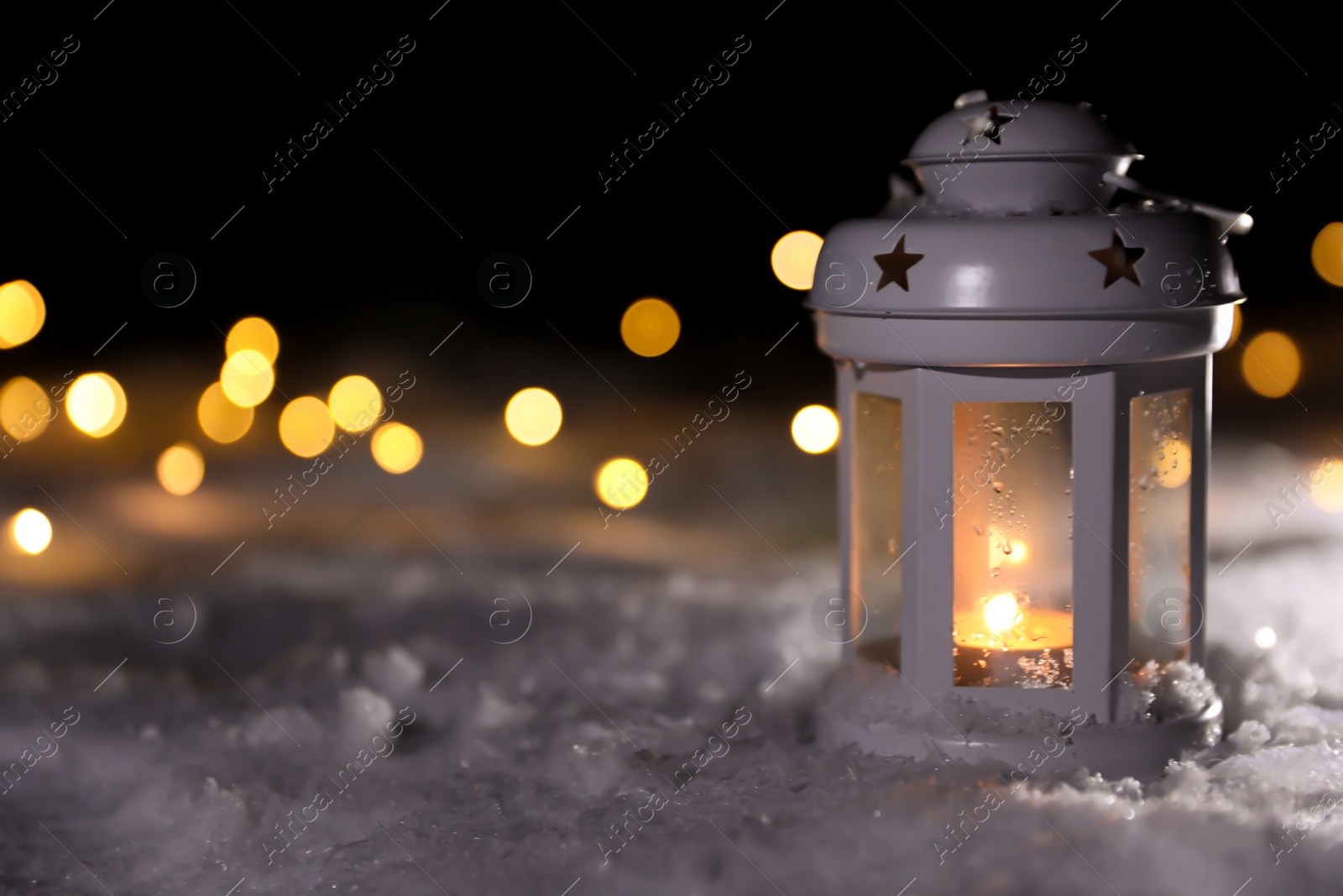 Photo of Lantern with burning candle and Christmas lights on white snow outdoors. Space for text