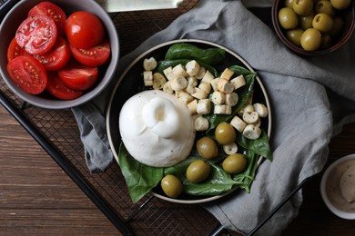 Delicious burrata cheese served with olives, croutons, basil and tomatoes on wooden table, top view