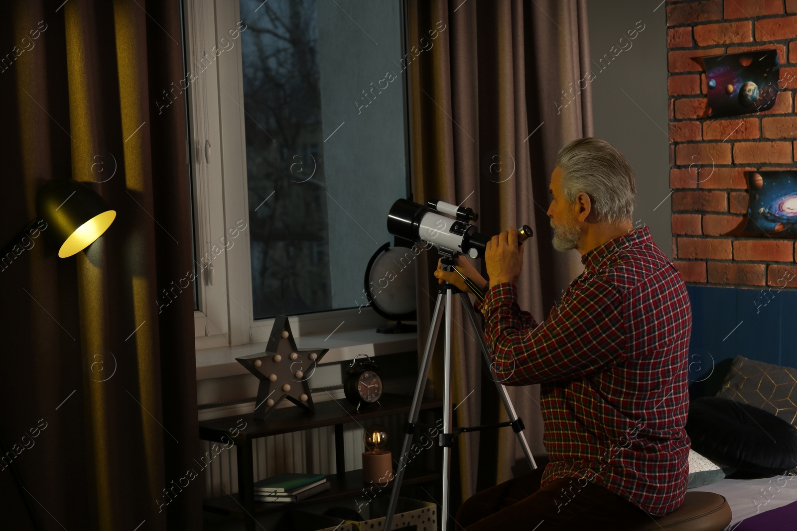 Photo of Senior man looking at stars through telescope in room