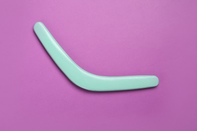 Photo of Turquoise wooden boomerang on purple background, top view