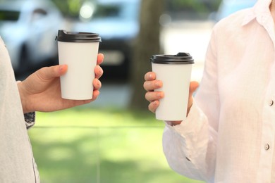 Women holding takeaway paper cups outdoors, closeup. Coffee to go