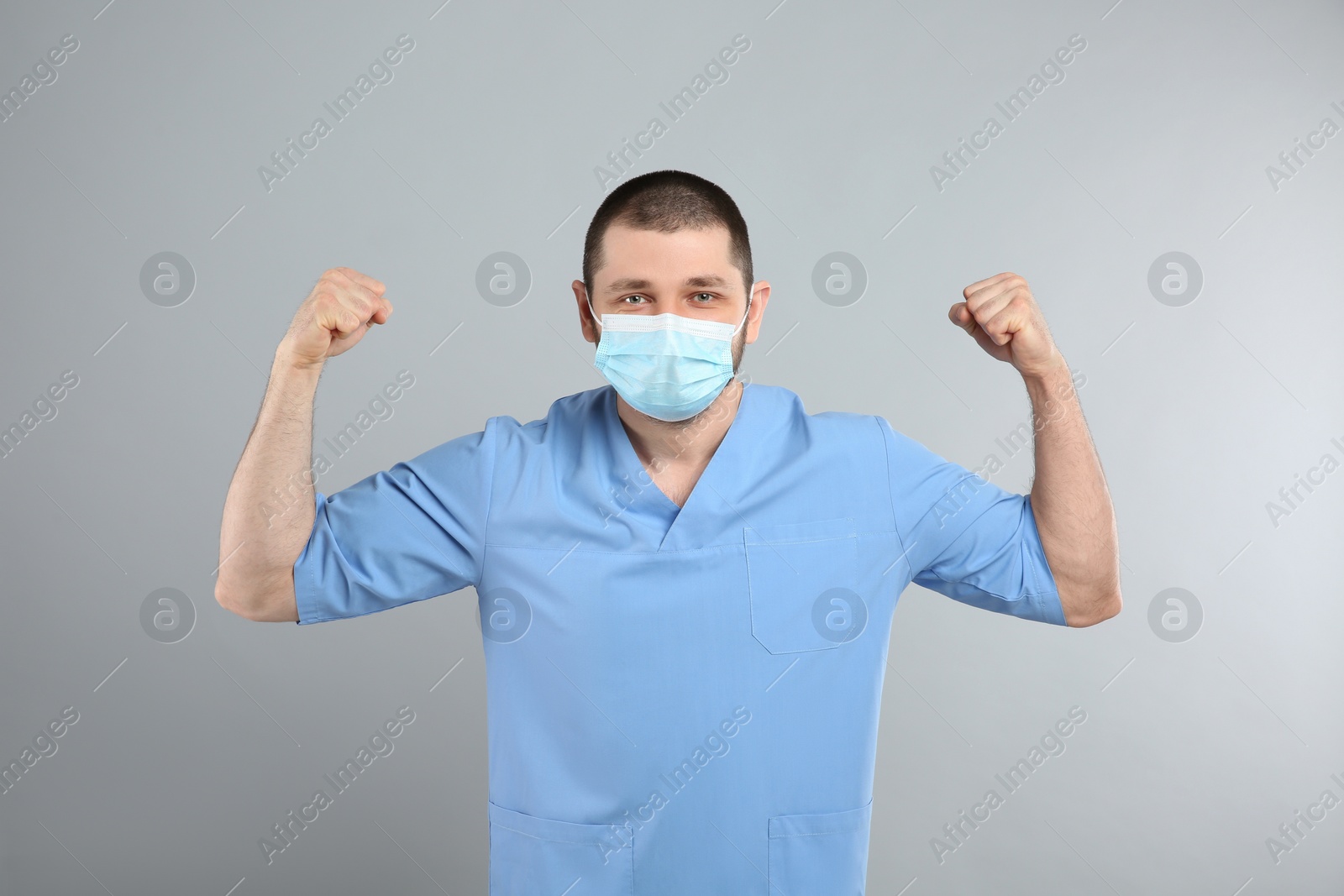 Photo of Doctor with protective mask showing muscles on light grey background. Strong immunity concept