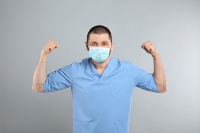 Doctor with protective mask showing muscles on light grey background. Strong immunity concept