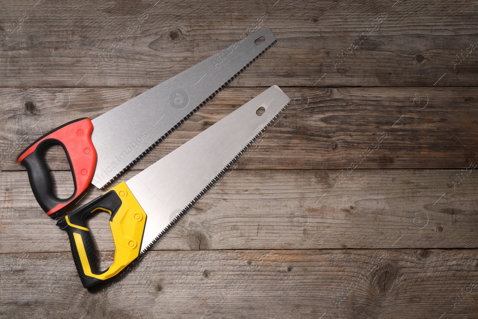 Photo of Saws with colorful handles on wooden background, flat lay. Space for text