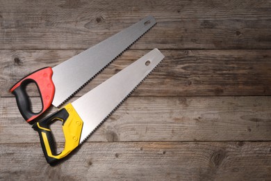 Saws with colorful handles on wooden background, flat lay. Space for text
