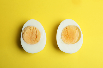 Photo of Halves of fresh hard boiled chicken egg on yellow background, flat lay