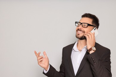 Handsome man in suit talking on smartphone against light grey background. Space for text