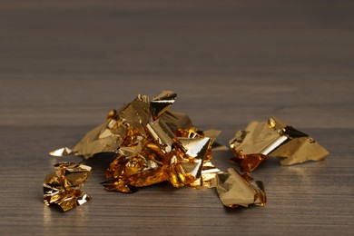 Photo of Pieces of edible gold leaf on wooden table, closeup. Space for text