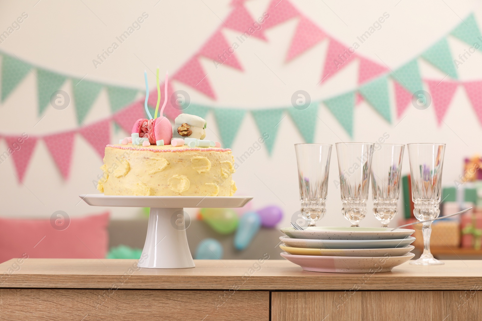 Photo of Delicious cake decorated with macarons and marshmallows and clean tableware on wooden table in festive room