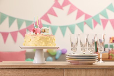 Photo of Delicious cake decorated with macarons and marshmallows and clean tableware on wooden table in festive room