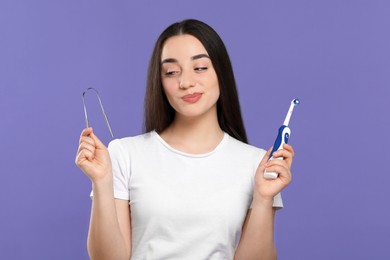 Photo of Woman with tongue cleaner and electric toothbrush on violet background
