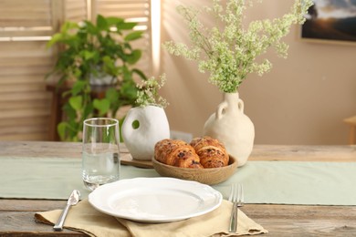 Photo of Clean tableware, flowers and fresh pastries on table in stylish dining room