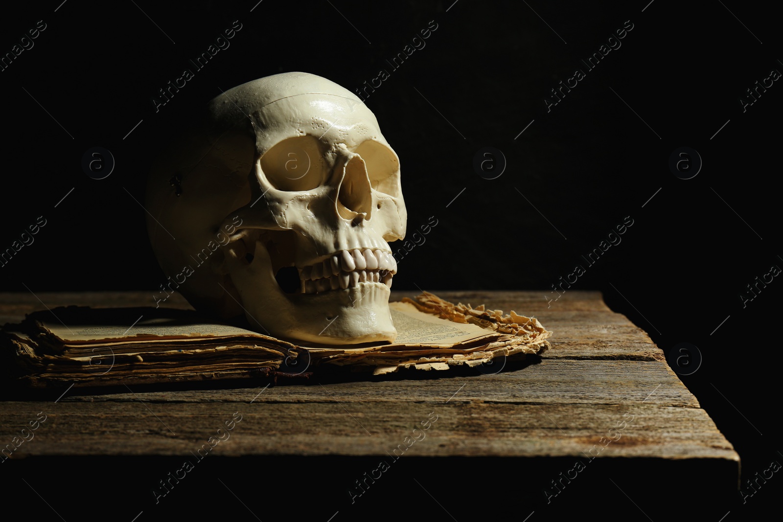 Photo of Human skull and old book on wooden table against black background, space for text